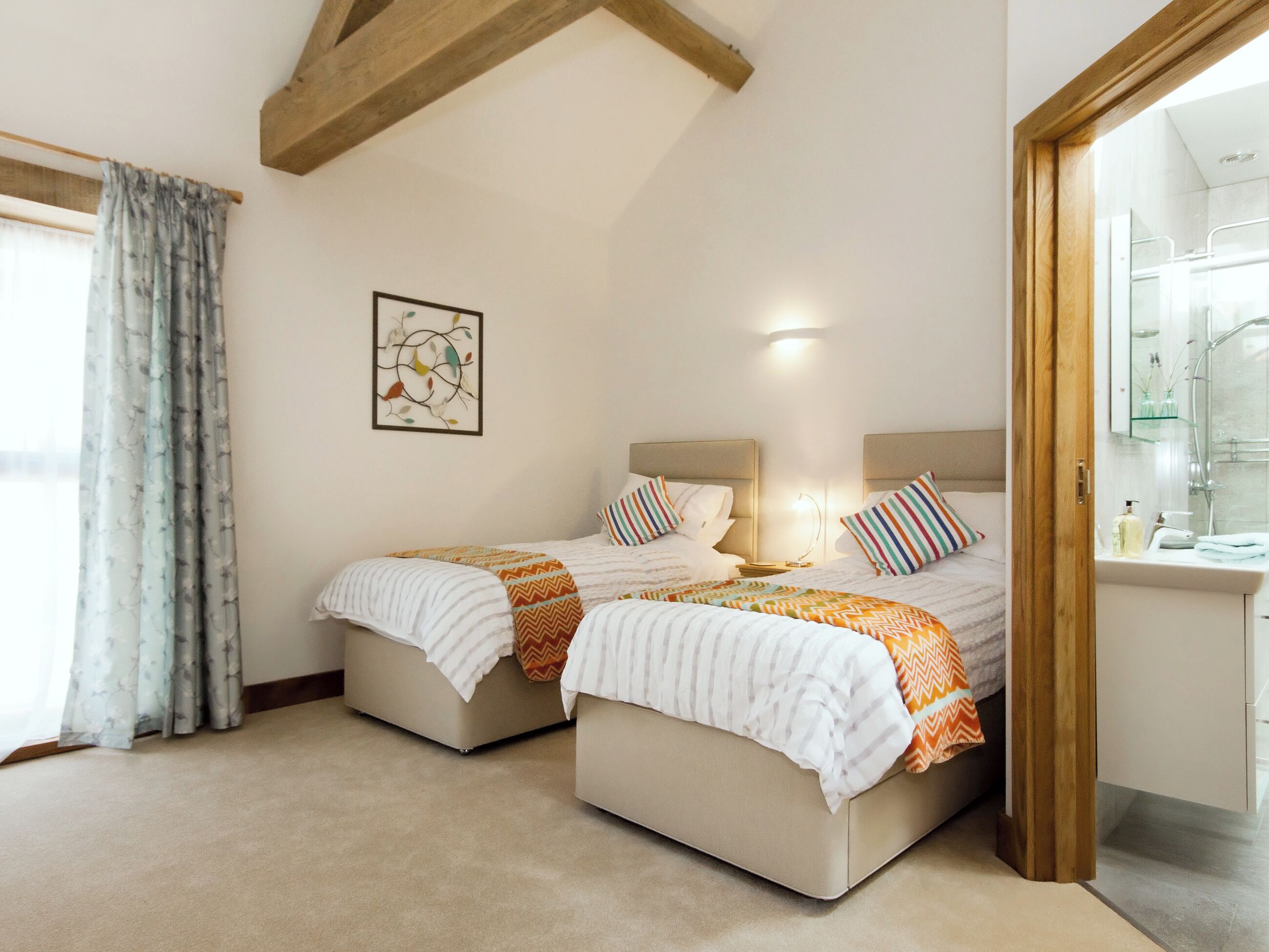 A hotel room with two beds, a bathroom with a glass shower, and a painting on the wall.