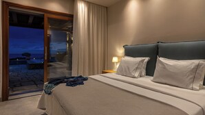 Ein Schlafzimmer mit einem großen Bett, einem Nachttisch mit Lampe und Blick ins Freie durch eine Schiebetür.