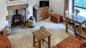 A cozy living room with a stone fireplace, a television, and a dining area with a table and chairs. - 1 Swallowholm Cottages (Arkengarthdale)