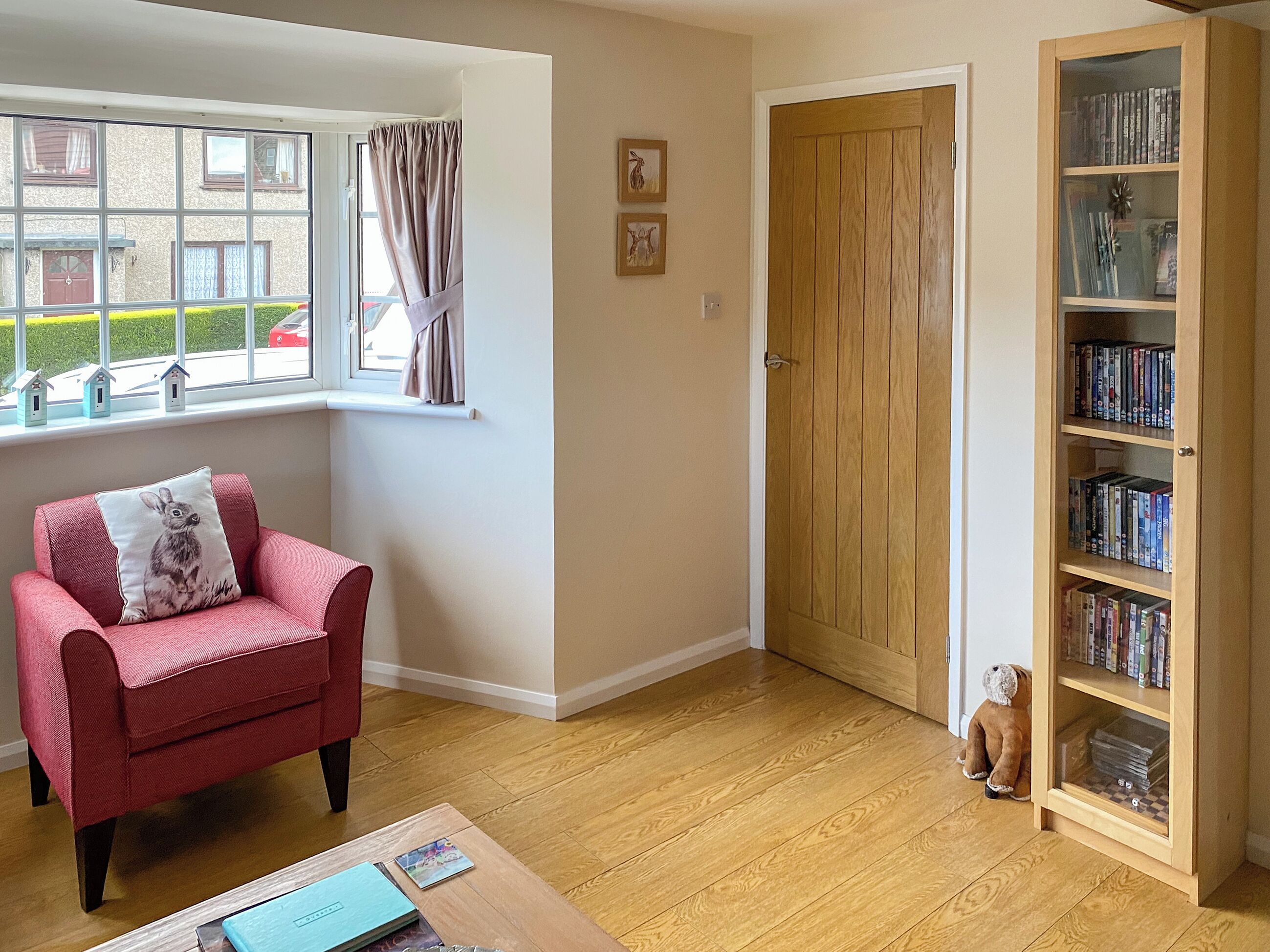 A cozy living room with a red armchair, a wooden bookshelf, and a window with curtains.