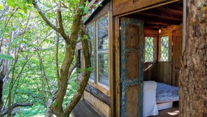 A rustic wooden cabin with a bed, large windows, and a view of the surrounding forest. - Hapus Hideaway Retreat Site, Sleeps 29 (Abergele)