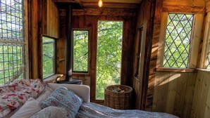 A wooden cabin bedroom with a bed, a desk, and a window with a view of trees. - Hapus Hideaway Retreat Site, Sleeps 29 (Abergele)