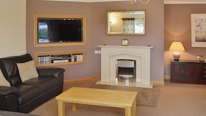 A living room with a fireplace, a sofa, a coffee table, a TV, and a bookshelf. - 4 bedroom accommodation in Red Row near Amble (Red Row near Amble)