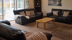 A living room with two black leather sofas, a wooden coffee table, and a patterned rug. - 4 bedroom accommodation in Red Row near Amble (Red Row near Amble)