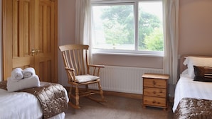 A bedroom with two beds, a wooden rocking chair, a wooden dresser, and a window with curtains. - 4 bedroom accommodation in Red Row near Amble (Red Row near Amble)