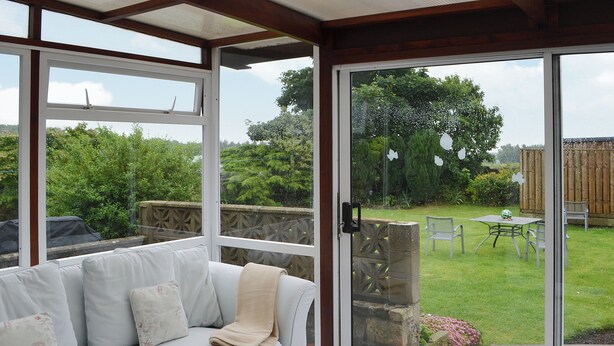 A conservatory with a white sofa and a glass door leading to a garden. - 4 bedroom accommodation in Red Row near Amble (Red Row near Amble)