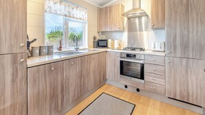 A modern kitchen with wooden cabinets, a stainless steel range hood, a built-in oven, and a window with a view of greenery.