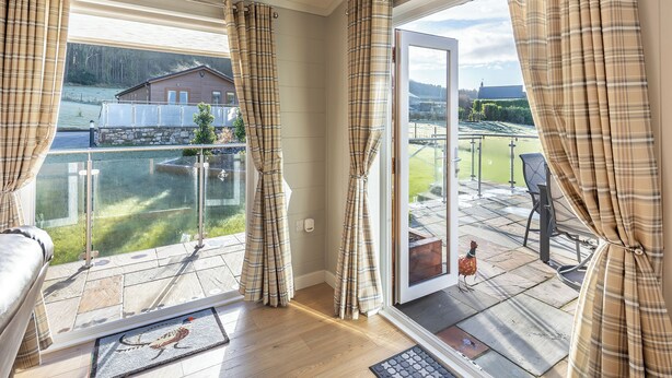 A room with a large window, a door leading outside, and a view of a house and a pond.