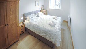 A bedroom with a bed, wooden wardrobe, bedside table, lamp, and a window.