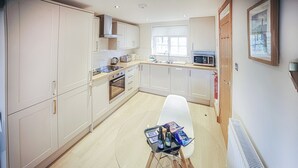 A modern kitchen with white cabinets, a glass table, and a white chair.