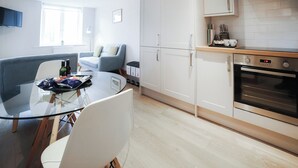 A modern kitchen with white cabinets, a built-in oven, and a dining area with a glass table and chairs.