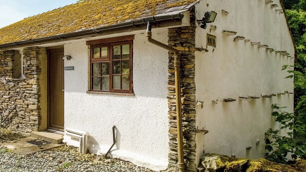 A small, white building with a stone foundation, a wooden door, and a window.