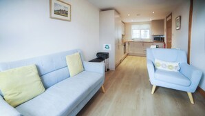 A living room with a light blue sofa and armchair, a small table, and a kitchen in the background.