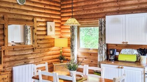 A wooden cabin interior with a dining table, chairs, a lamp, a window, and kitchen cabinets. - 3 bedroom accommodation in Llanfynydd (Llanfynydd)