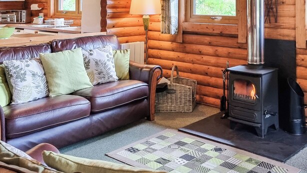 A log cabin interior with a leather sofa, a fireplace, a dining area, and a view of the outdoors. - 3 bedroom accommodation in Llanfynydd (Llanfynydd)
