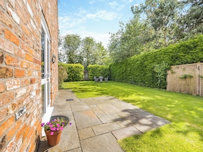 A brick building with a window, a paved patio, and a well-maintained lawn.