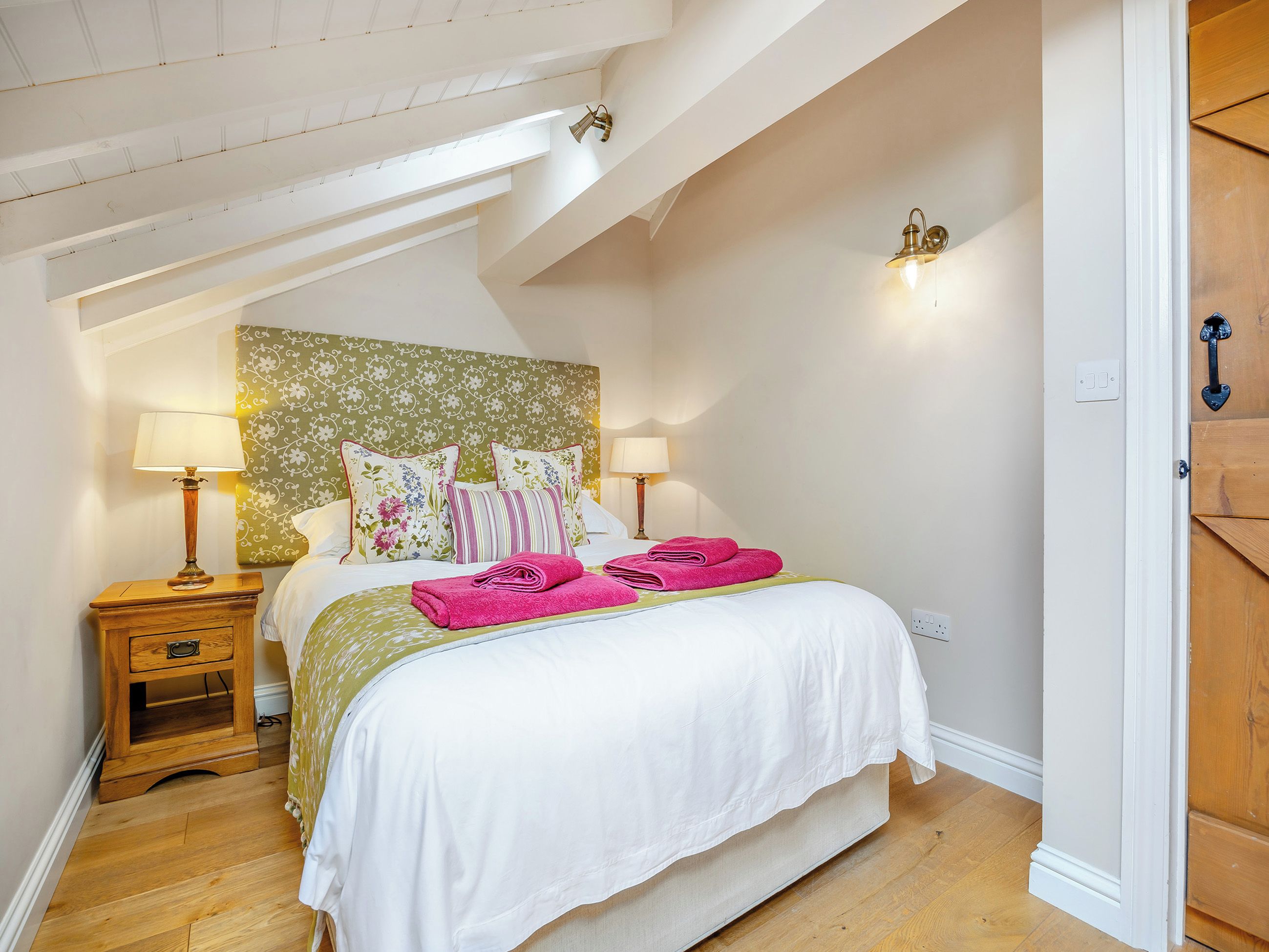 Een slaapkamer met een bed, twee nachtkastjes, een hoofdbord en een houten deur.