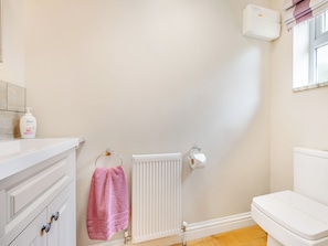 A bathroom with a white toilet, a radiator, a pink towel, and a bottle of Dove soap on a counter.