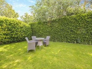 A garden with a table and four chairs, surrounded by well-maintained hedges and grass.