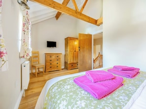 A bedroom with a bed, wooden furniture, a television, and a staircase.