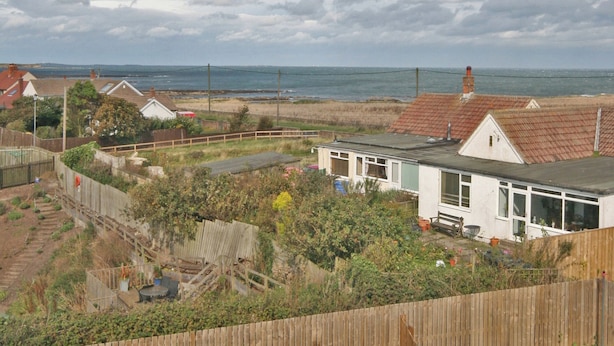 A residential area with a house featuring a large window, a fenced yard, and a view of the sea. - 3 bedroom accommodation in Beadnell (Beadnell)