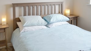 A bedroom with a wooden headboard, two bedside tables with lamps, and a bed with white and light blue bedding. - 3 bedroom accommodation in Beadnell (Beadnell)