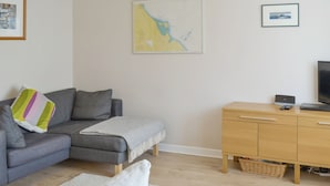 A modern living room with a grey sofa, a white sofa, a wooden cabinet, and a television. - 3 bedroom accommodation in Beadnell (Beadnell)