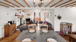 A dining area with a table set for two, wooden chairs, a chandelier, and a bookshelf.
