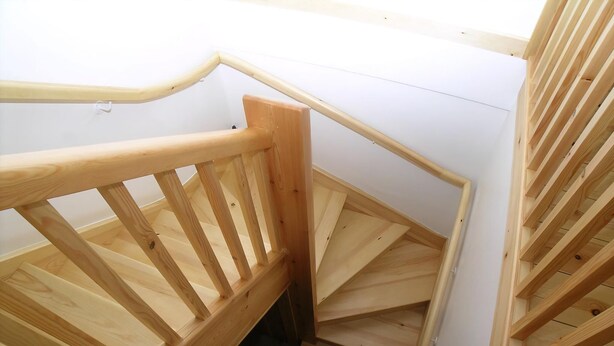 A wooden spiral staircase with a handrail and open riser design.