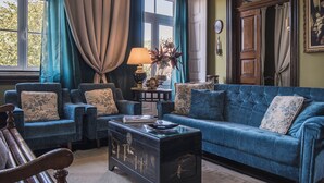 Un salon avec un canapé bleu, deux fauteuils, une table basse en bois et une lampe.