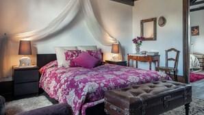 Une chambre à coucher avec un grand lit, une table de chevet, une chaise en bois et une petite table avec une lampe.