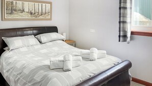 Een net opgemaakt bed met een geborduurd sprei, hoofdbord en nachtkastje met een lamp.