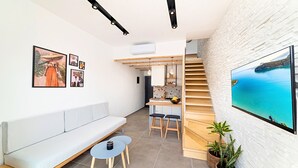 Un espacio de estar moderno con sofá, zona de comedor y escalera que conduce a un nivel superior.