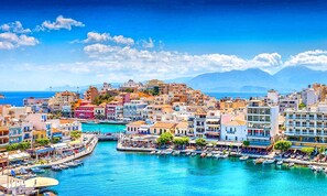 A coastal town with buildings along a waterfront, boats docked, and a clear blue sky. - Aelia Suite Private Pool (Istro)