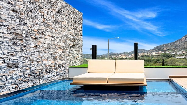 Una piscina con un muro de piedra y un sofá color beige.
