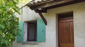 Un edificio rústico con puerta de madera y ventana con contraventanas verdes.