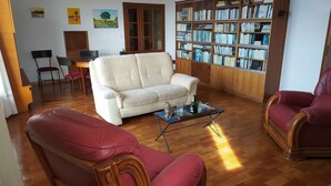 Una sala de estar con un sofá blanco, sillas de cuero rojo, una mesa de centro y una estantería llena de libros.