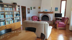 Una sala de estar con chimenea, sillones de cuero, un sofá, una estantería de madera y un televisor.