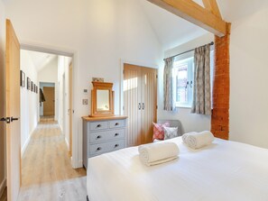 Een slaapkamer met een bed, een dressoir, een spiegel en een raam met gordijnen.
