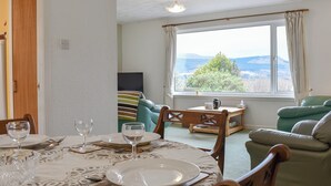Un comedor con una mesa dispuesta para cuatro personas, un sofá y una ventana que ofrece vistas a zonas verdes y montañas.