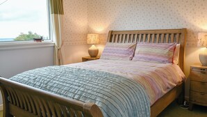 Un dormitorio con una cama de madera, ropa de cama estampada, una mesita de noche con lámpara y una ventana con cortinas.
