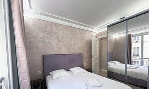 A hotel room with a large bed, a bedside table, a mirror, and a view of the outside. - Urban Flat 180 - Nice Apartment in the center of Le Marais district (París)