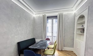 Une piÚce comprenant une table en marbre, deux chaises, un canapé, un balcon avec une balustrade et une étagÚre blanche.