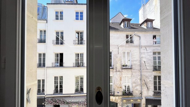 A view through a window of a building with multiple balconies, a door with a brass handle, and a sign that reads 'DURACCE'.