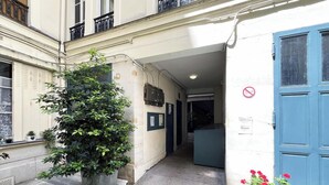 A narrow alleyway with a large potted plant, a blue door, and a sign indicating a no smoking area.