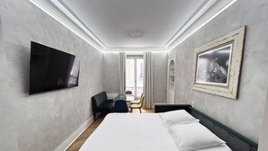 A hotel room with a bed, a flat-screen TV, a desk with a chair, and a balcony with a view.