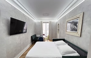 Habitación de hotel con cama, televisor de pantalla plana, escritorio con silla y balcón con vistas.