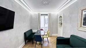 A room with a dining table, chairs, a green sofa, a TV, and a balcony with a railing.