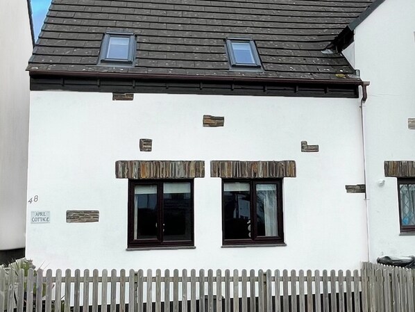 A white building with two windows, a wooden picket fence, and a small sign reading "APRIL COTTAGE". - 2 bedroom accommodation in Padstow (Padstow)
