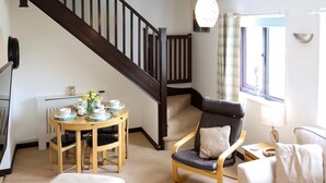 Een gezellige woonkamer met een houten eettafel gedekt voor vier personen, een leren fauteuil, een bank en een trap naar een ander niveau.